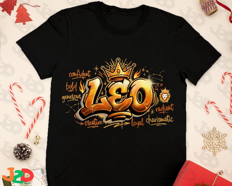 May include: Black t-shirt featuring a gold and orange graphic design with the word "LEO" in a graffiti style. The design includes a crown, constellation, and words like "confident" and "creative".