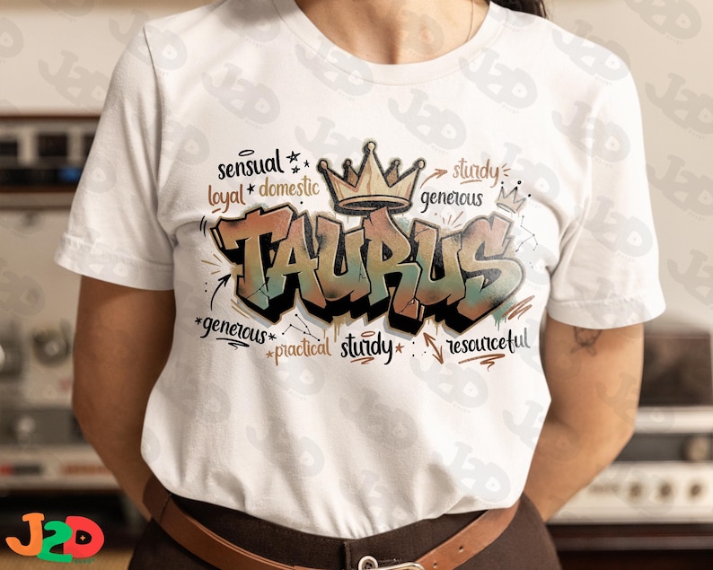 May include: White t-shirt featuring the word "TAURUS" in a graffiti style with a crown above it. The design includes words like "sensual", "loyal", "generous", and "resourceful".