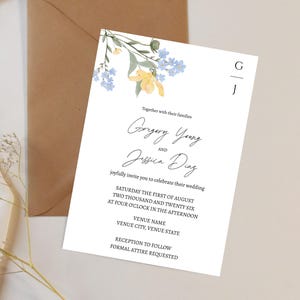 May include: A white wedding invitation with floral details and a brown envelope. The invitation includes the names "Gregory Young" and "Jessica Diaz", along with wedding details. The invitation is decorated with yellow and blue flowers.
