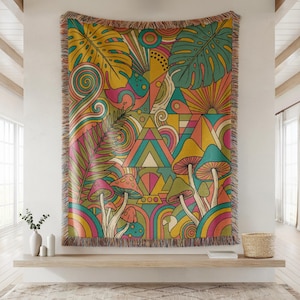 May include: A rectangular woven throw blanket featuring a vibrant, multi-colored graphic pattern of mushrooms, large tropical leaves, geometric triangles, and swirling lines. The edges are finished with a decorative, multi-colored fringe border.
