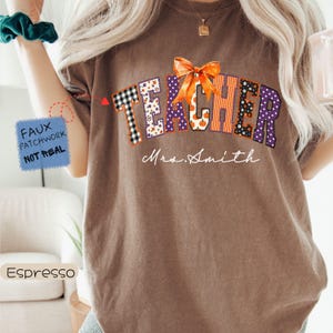 May include: An espresso-colored t-shirt featuring the word TEACHER in a faux patchwork design with various patterns, topped with an orange bow graphic. Below the word, the text Mrs. Smith is printed in white script. A blue box notes faux patchwork.