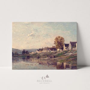 Puede incluir: Una impresión de paisaje vintage que representa una serena escena fluvial con un pueblo en la orilla. La obra de arte presenta colores suaves, un cielo nublado y reflejos en el agua. La impresión tiene el texto "BLUEBELL ART PRINTS" en la parte inferior.