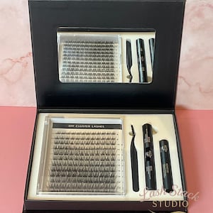 Könnte beinhalten: Eine schwarze Box mit DIY-Wimpern, einer Pinzette, Wimpernversiegelung und Entferner. Die Box ist geöffnet und zeigt den Inhalt, der ordentlich angeordnet ist. Der Text "DIY Cluster Lashes" ist auf einem der Behälter zu sehen.