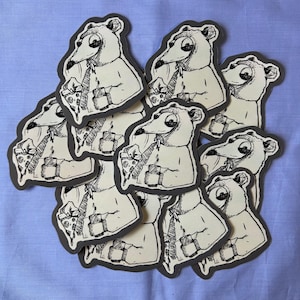 May include: A collection of stickers featuring a cartoon bear character in a suit and tie, holding a slice of pizza and a coffee cup. The stickers have a white background with a dark gray border, set against a light blue backdrop.
