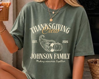 May include: An olive green short-sleeve t-shirt featuring the text "THANKSGIVING Crew" in white and gold, "EST. 2026" in white, a cornucopia graphic, and the text "JOHNSON FAMILY" with "Making memories together" in white lettering.