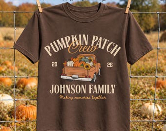 May include: A dark brown short-sleeve t-shirt featuring a graphic of an orange pickup truck filled with pumpkins and sunflowers. The text reads PUMPKIN PATCH CREW, 20 26, JOHNSON FAMILY, and Making memories together in cream-colored lettering.