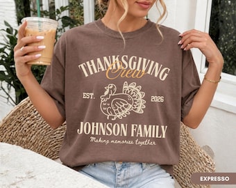 May include: A brown short-sleeve t-shirt featuring a graphic with the text "THANKSGIVING Crew", "EST. 2026", "JOHNSON FAMILY", and "Making memories together". The design includes a central illustration of a turkey in a light cream color.