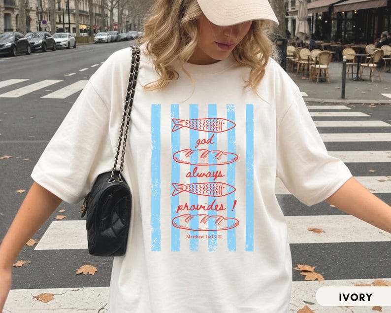 Woman wearing oversized Comfort Colors Christians shirt featuring God Always Provides graphic with fish illustrations and Matthew 14:13-21 Bible verse in vintage aesthetic style.