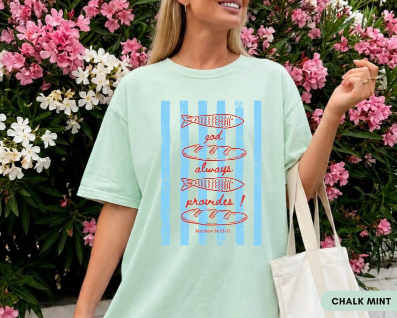 Woman wearing oversized Comfort Colors Christians shirt featuring God Always Provides graphic with fish illustrations and Matthew 14:13-21 Bible verse in vintage aesthetic style.