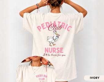 May include: An ivory t-shirt featuring a back graphic of a goose wearing a nurse cap and holding a clipboard with the text PEDIATRIC CLUB NURSE I'll be there for you. The front chest area displays the text PEDS RN CLUB est. 22.26 in pink lettering.