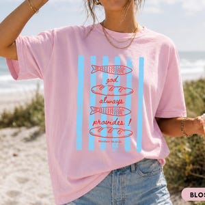 Woman wearing oversized Comfort Colors Christians shirt featuring God Always Provides graphic with fish illustrations and Matthew 14:13-21 Bible verse in vintage aesthetic style.