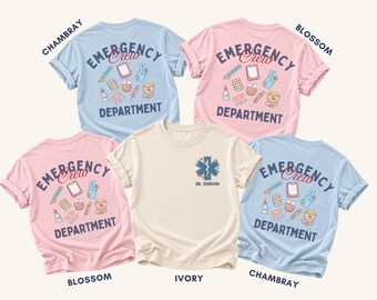 May include: Five short-sleeve t-shirts in chambray blue, blossom pink, and ivory. Four shirts feature a back graphic with medical icons and the text EMERGENCY CREW DEPARTMENT. One ivory shirt features a front chest logo with a medical star.