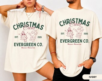 May include: An ivory short-sleeve t-shirt featuring the dark green text CHRISTMAS EVERGREEN CO. and the maroon script text Crew and Human Resources. A graphic shows a Santa Claus and a decorated tree with the text EST. 2026.