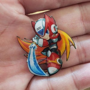 Puede incluir: Un colorido pin de esmalte con el personaje Zero de la serie Mega Man X. El pin representa a Zero, un robot rojo y blanco con una espada de energía azul. El pin tiene un fondo amarillo y naranja.