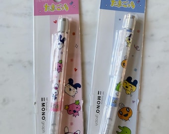 May include: Two Tombow MONO graph 0.5 mm mechanical pencils in original packaging. The left pencil features pink accents and Tamagotchi character graphics, while the right pencil has blue accents and various colorful Tamagotchi character prints.