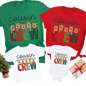 May include: A collection of four shirts and a bodysuit in red, green, and white. Each garment features the text "cousin CREW" in a dark green script and bold red and green block letters, accompanied by a graphic of five reindeer wearing scarves.
