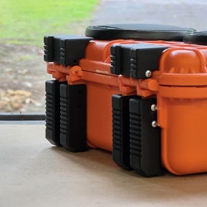 Può includere: Due valigie rettangolari arancioni con dettagli e chiusure neri. Le valigie hanno una superficie strutturata e sono progettate per proteggere il contenuto. Sono su una superficie chiara, con uno sfondo esterno sfocato.