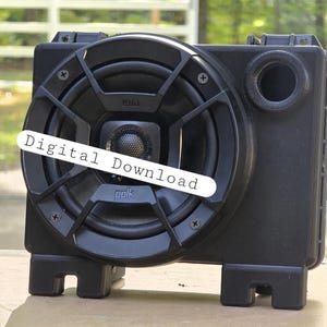 May include: A black speaker with a circular speaker grill and the text "polk" visible. The speaker has a rectangular body with a port on the side and the words "Digital Download" on a white banner across the front.
