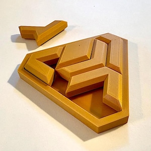 May include: A tan-colored, geometric puzzle with several interlocking pieces. The puzzle has a shield-like shape with a raised border. One piece is separate, while the others fit within the frame. The pieces have a textured surface, suggesting a 3D-printed design.
