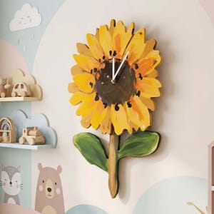 Pode incluir: Um relógio de parede em forma de girassol com pétalas amarelas, um centro castanho escuro e folhas verdes. O relógio tem ponteiros brancos e está montado numa parede de cor clara. O relógio é um item decorativo para o quarto de uma criança.
