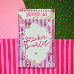 May include: A spiral-bound sticker booklet titled "Sticker Booklet Vol. 1" with a pink and blue striped cover. The cover features the text "Ethereal Craft Studio" and includes various sticker illustrations and the text "Over 250 Stickers". The background is pink and green fabric.