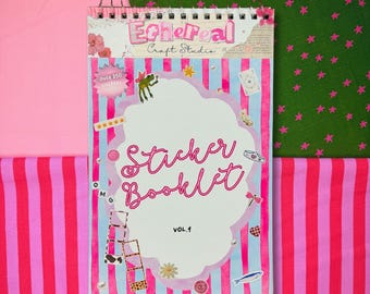 May include: A spiral-bound sticker booklet titled "Sticker Booklet Vol. 1" with a pink and blue striped cover. The cover features the text "Ethereal Craft Studio" and includes various sticker illustrations and the text "Over 250 Stickers". The background is pink and green fabric.