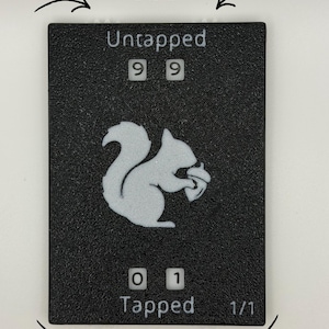 May include: Black rectangular game piece with white text and a squirrel graphic. The text reads "Untapped" with dials showing "99", and "Tapped" with dials showing "01". The bottom right corner reads "1/1".
