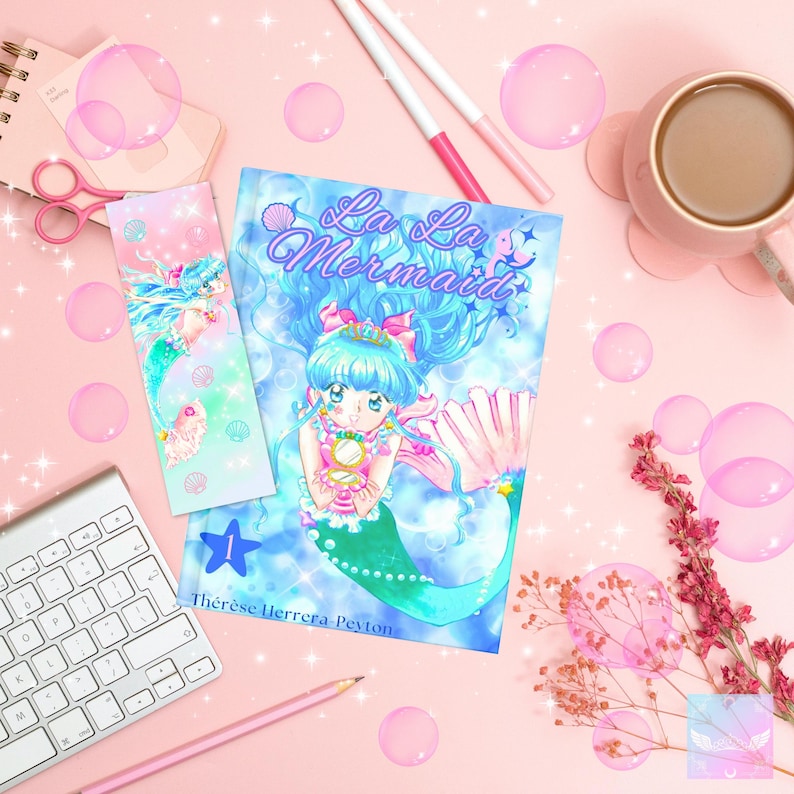 Puede incluir: Ilustraci&oacute;n colorida de una sirena en la portada de un libro y un marcap&aacute;ginas, con el t&iacute;tulo "La La Mermaid". La sirena tiene el pelo azul y la cola verde. Burbujas rosas y art&iacute;culos de papeler&iacute;a rodean el libro sobre una superficie rosa.