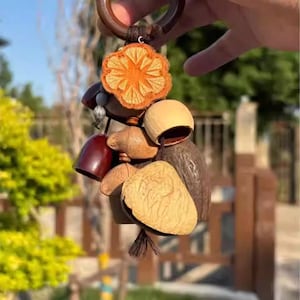 May include: A wooden keychain with a selection of natural elements. The keychain includes a carved orange flower, beads, and several uniquely shaped wooden pieces in shades of brown and tan. A dark brown wooden ring serves as the key ring.