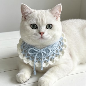 Può includere: Un collare per animali all'uncinetto color azzurro e crema con un delicato bordo smerlato e un dettaglio a fiocco centrale. Il collare è realizzato con un motivo circolare e include lunghi lacci sottili che pendono dal centro del girocollo.