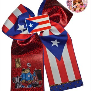 Puede incluir: Un gran lazo para el cabello patriótico con el diseño de la bandera puertorriqueña en rojo, blanco y azul. El lazo incluye un pequeño emblema de la bandera y un centro rojo brillante. También aparece una rana de dibujos animados con una bandera puertorriqueña.