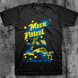 May include: Black t-shirt with a yellow and blue graphic of a futuristic vehicle with the text "Moon Patrol" above it.