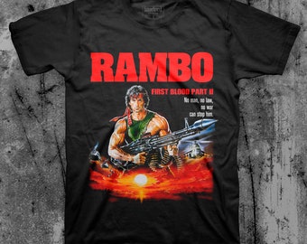 Może przedstawiać: Czarny T-shirt z czerwoną grafiką Johna Rambo z filmu "First Blood Part II". Grafika przedstawia Rambo trzymającego karabin maszynowy na tle zachodu słońca. Tekst "RAMBO" jest czerwony, a tekst "FIRST BLOOD PART II" jest biały. Tekst "No man, no law, no war can stop him." jest biały.