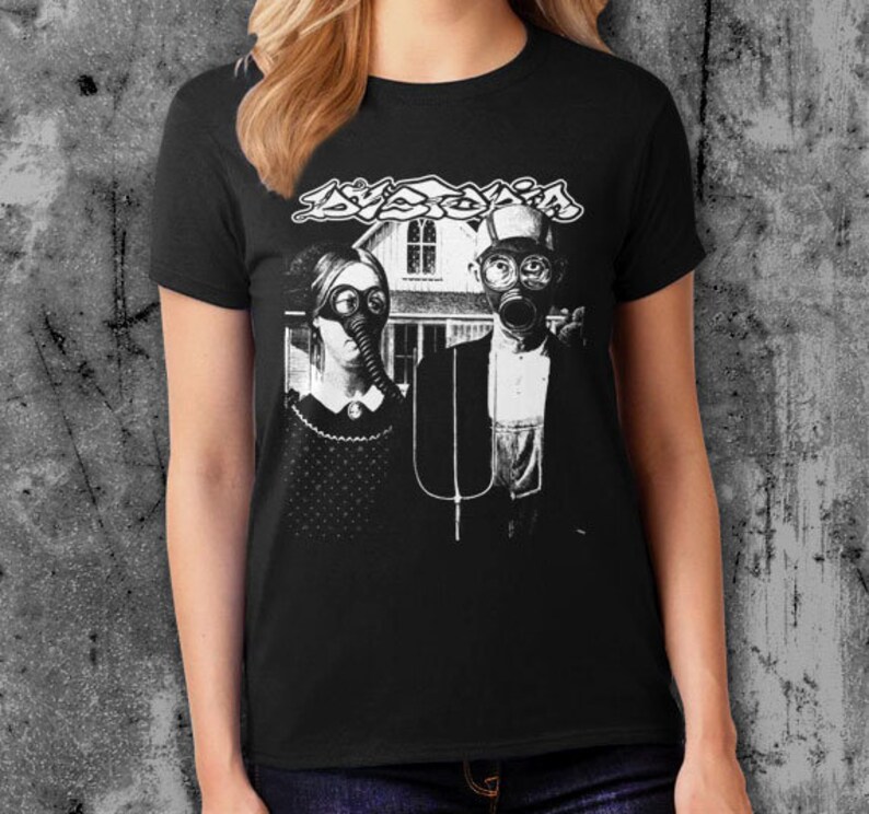 Puede incluir: Camiseta negra con un gr&aacute;fico en blanco y negro de una pareja con m&aacute;scaras de gas, una casa y la palabra "Dyslexia". El dise&ntilde;o es una parodia de la pintura American Gothic.