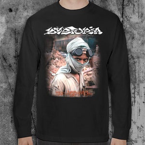K&ouml;nnte beinhalten: Schwarzes Langarm-T-Shirt mit einem Grafikdruck einer Person mit Gesichtsmaske und Schutzbrille. Der Text "Dystopia" ist in Wei&szlig; auf dem Shirt gedruckt.