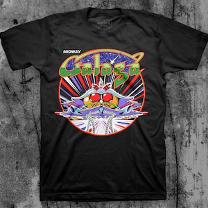 May include: Black t-shirt with a colorful graphic of a spaceship from the classic arcade game Galaga. The graphic includes the text "MIDWAY" and "Galaga".
