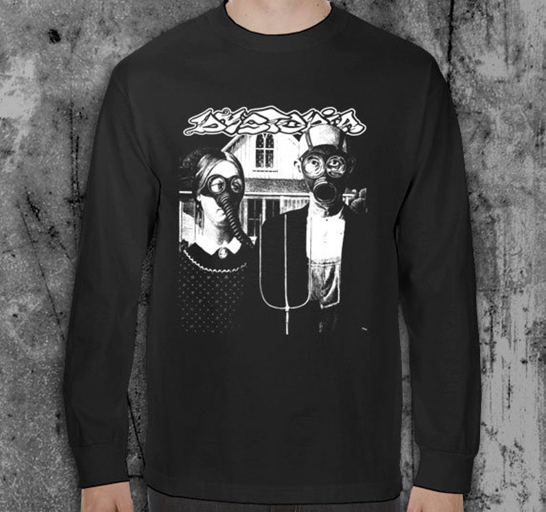 Puede incluir: Camiseta negra de manga larga con un gr&aacute;fico en blanco y negro. El gr&aacute;fico muestra dos figuras con m&aacute;scaras de gas frente a una casa, con la palabra "AVOXIA" encima. La camiseta es de material suave.