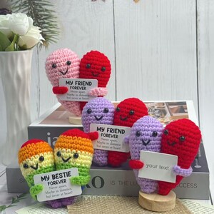 May include: Crocheted heart-shaped figures in various colors, including pink, red, purple, and rainbow hues. Each figure holds a small sign with the text "MY FRIEND FOREVER" or "MY BESTIE FOREVER". The figures are displayed on a white surface.