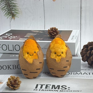 May include: Two plush sweet potato toys with smiling faces. The toys are brown and orange, with a cute, cartoonish design. The background includes books and pinecones.