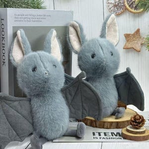 May include: Two plush gray bat stuffed animals with large ears and outstretched wings. The bats are sitting on wooden slices. The text on the book says "As people are living a better life now, they are getting more and more attentive to their hairstyles."