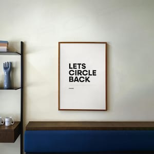May include: A framed print with the text "LETS CIRCLE BACK" in bold black letters on a white background. The frame is a warm brown color, and the print is hanging on a cream-colored wall. Below the print is a blue bench.
