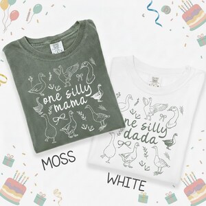 Puede incluir: Se muestran dos camisetas, una verde musgo y otra blanca. La camiseta verde musgo tiene el texto "one silly mama" y la camiseta blanca tiene el texto "one silly dada". Ambas camisetas presentan un gr&aacute;fico de ganso.