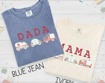Puede incluir: Dos camisetas, una azul vaquero y otra marfil, con las palabras "DADA" y "MAMA" en rojo. Cada camiseta tiene gráficos bordados de vehículos de emergencia: una ambulancia, un coche de policía y un camión de bomberos. La camiseta azul vaquero tiene el texto "BLUE JEAN" y la camiseta marfil tiene el texto "IVORY".