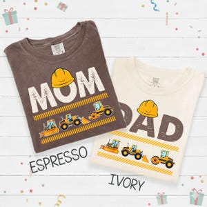 May include: Two t-shirts, one espresso and one ivory, with construction-themed designs. The espresso shirt says "MOM" with a yellow hard hat and construction vehicles. The ivory shirt says "DAD" with a yellow hard hat and construction vehicles.