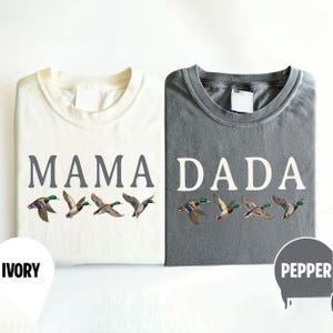 Pu&ograve; includere: Due magliette a girocollo, una color avorio e una grigio pepe, entrambe con la grafica di quattro germani reali in volo. La maglietta avorio riporta la scritta MAMA in grigio, mentre quella grigio pepe riporta la scritta DADA in bianco.