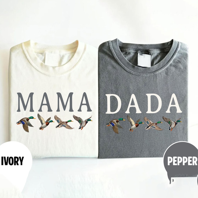 Pu&ograve; includere: Due magliette a girocollo, una color avorio e una grigio pepe, entrambe con la grafica di quattro germani reali in volo. La maglietta avorio riporta la scritta MAMA in grigio, mentre quella grigio pepe riporta la scritta DADA in bianco.