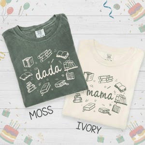 May include: Two t-shirts, one moss green and one ivory, with book illustrations. The moss green shirt says "dada" and the ivory shirt says "mama". Both shirts have a crew neck and short sleeves.