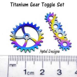 May include: A set of two titanium gears with a rainbow iridescent finish. The larger gear is approximately 1 cm in diameter and has 24 teeth. The smaller gear is a chain of 5 gears, each with 12 teeth. The gears are made of titanium and have a rainbow iridescent finish.