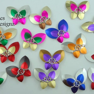 May include: Assortment of colorful metal butterfly charms with a variety of colors including red, orange, yellow, green, blue, purple, and silver. Butterflies Metal Designz is written in the top left corner of the image.