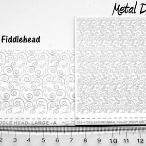May include: Two white sheets of decorative metal with a swirling pattern. The sheets are labeled "Fiddlehead" and "Metal Designz". The larger sheet measures 2.5 inches by 6 inches and the smaller sheet measures 3 inches by 4 inches.